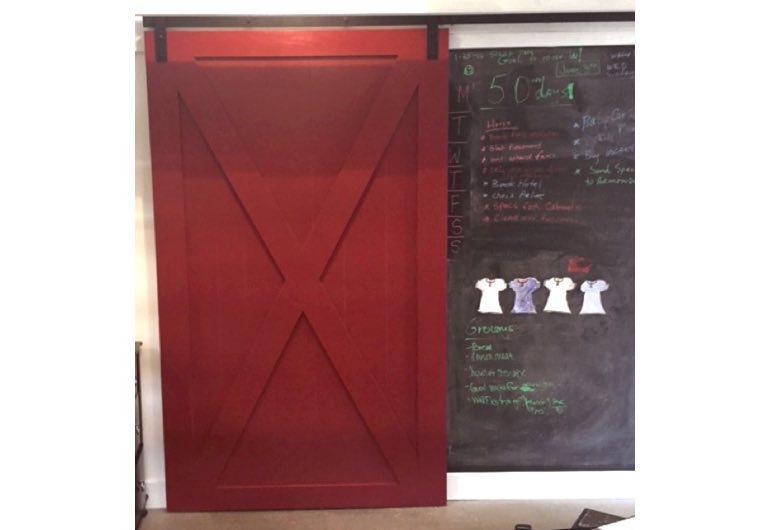 Red x-frame sliding barn door with black track next to chalkboard 
